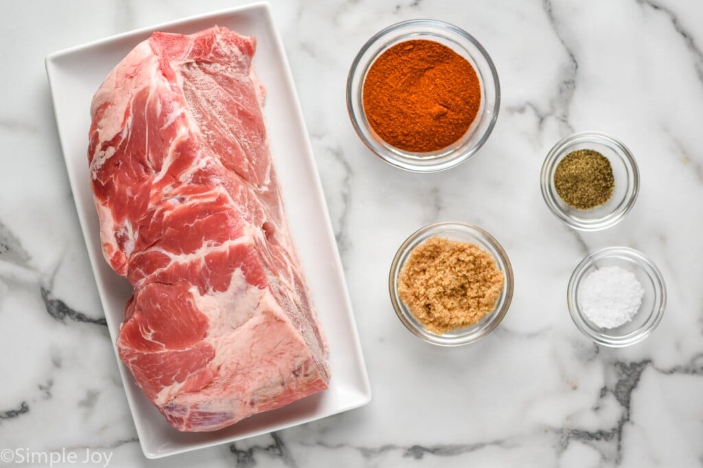 Overhead view of raw pork shoulder and small bowls of seasonings on countertop for Crock Pot Pulled Pork recipe.