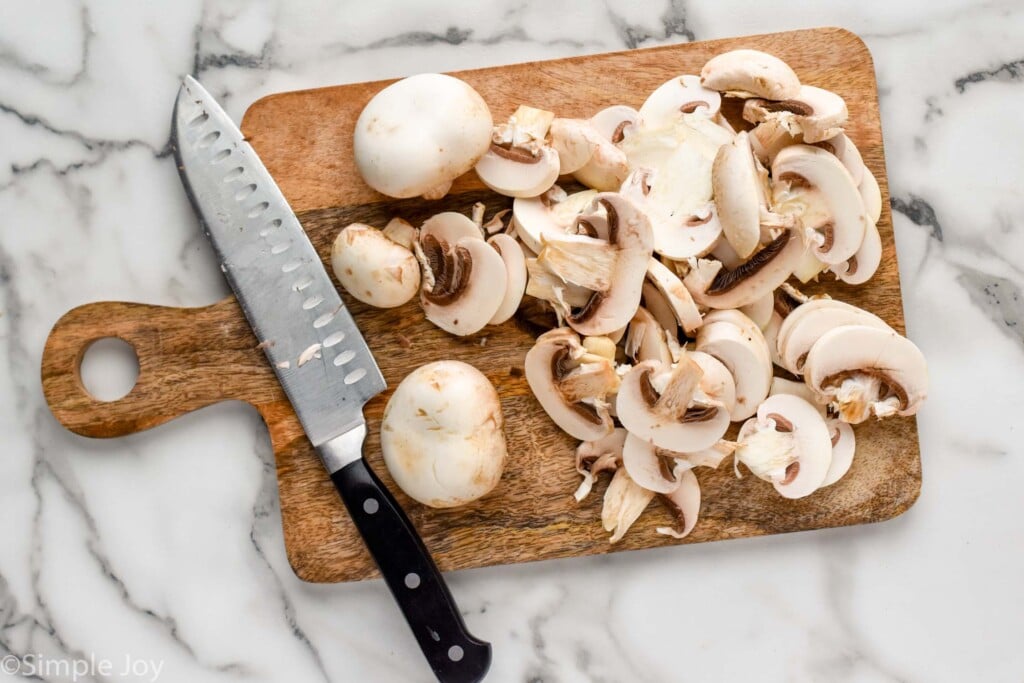 Overhead view of a cutting board with sliced raw mushrooms and a knife for Sautéed Mushrooms recipe