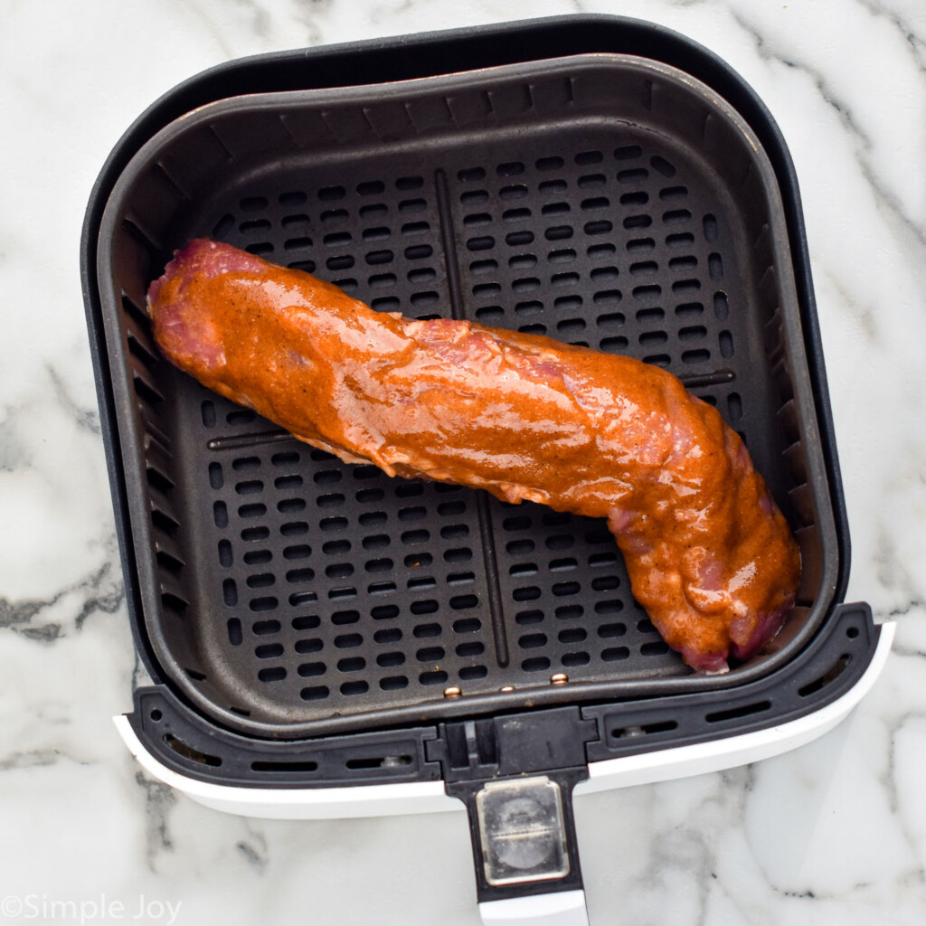 Overhead view of pork tenderloin covered in sauce for Air Fryer Pork Tenderloin in air fryer basket before cooking.