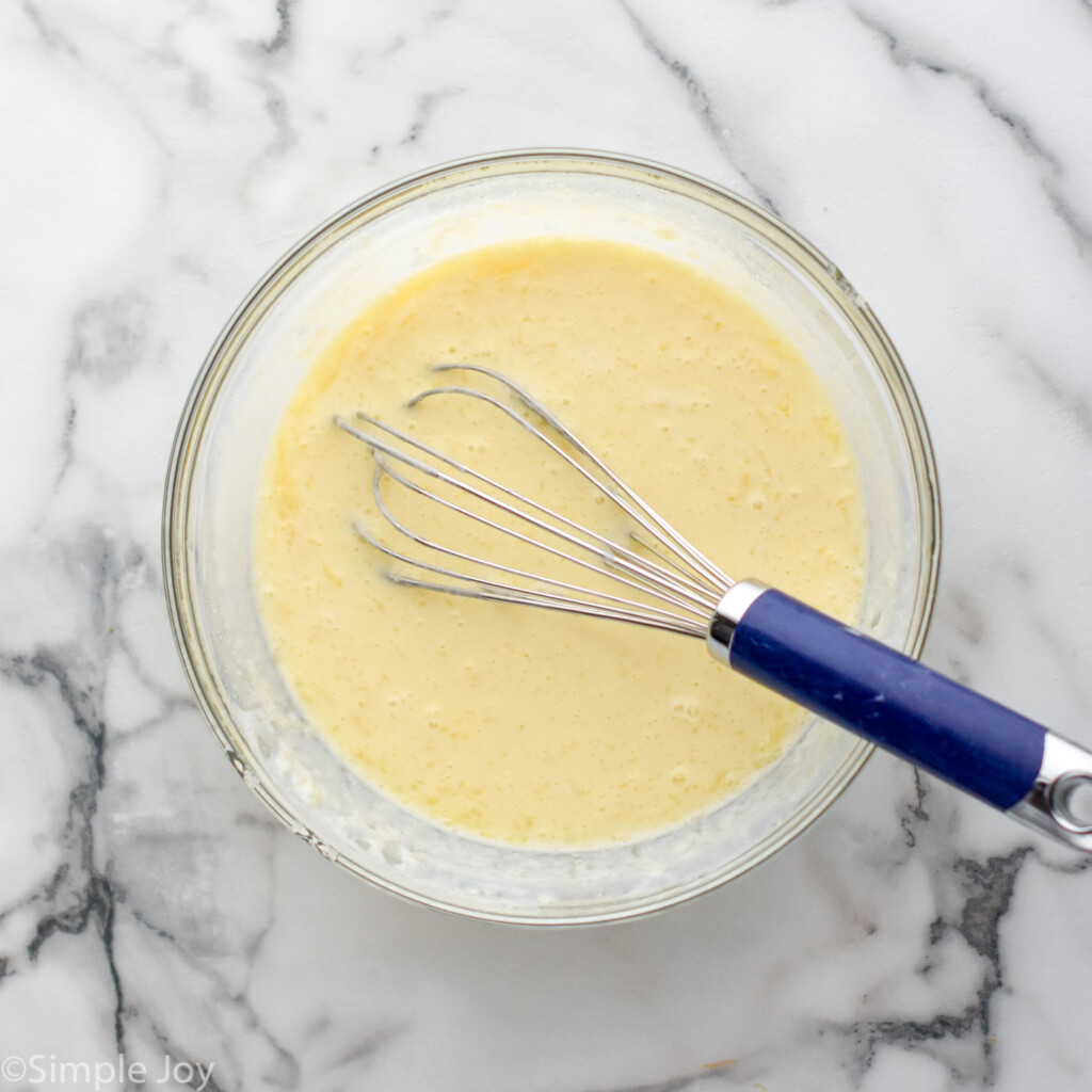 Overhead view of batter for Sheet Pan Pancakes recipe in a glass mixing bowl with whisk.