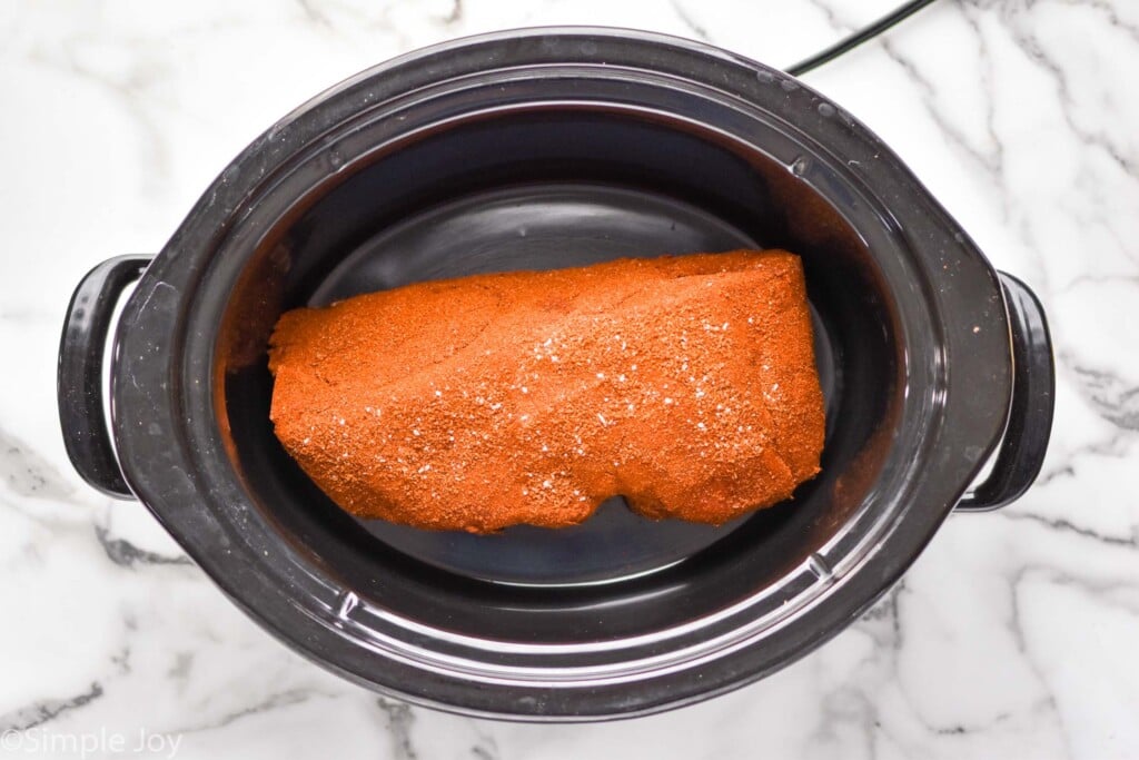 Overhead view of a slow cooker with seasoned pork shoulder for Crock Pot Pulled Pork recipe