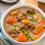 Bowl of Crockpot Beef Stew with silverware and a glass of red wine beside - 10