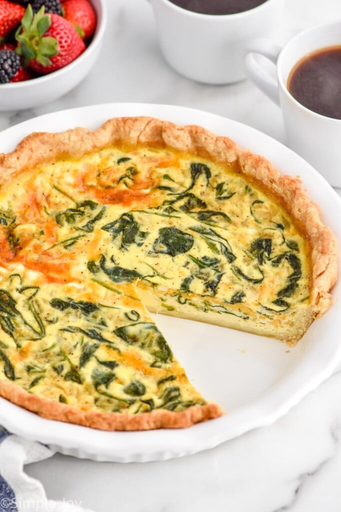 Spinach Quiche with one piece removed. Cups of coffee and bowl of berries beside.