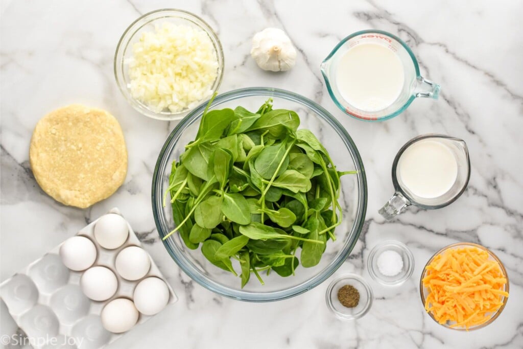 Overhead view ingredients measured out in individual dishes on countertop for Spinach Quiche recipe.