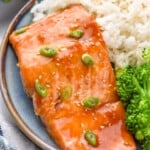 Teriyaki Salmon garnished with green onions and sesame seeds, served on a plate with white rice and broccoli. Fork beside. - 9