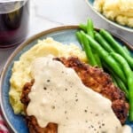 Pinterest graphic for Chicken Fried Steak. Says "the best chicken fried steak simplejoy.com" Image shows a plate of Chicken Fried Steak topped with gravy, mashed potatoes, and green beans.