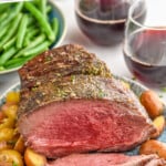 Pinterest graphic for Sirloin Tip Roast recipe. Text says, "the best Sirloin Tip Roast simplejoy.com." Image shows a platter with sliced Sirloin Tip Roast and potatoes. Glasses of red wine and bowl of green beans beside.