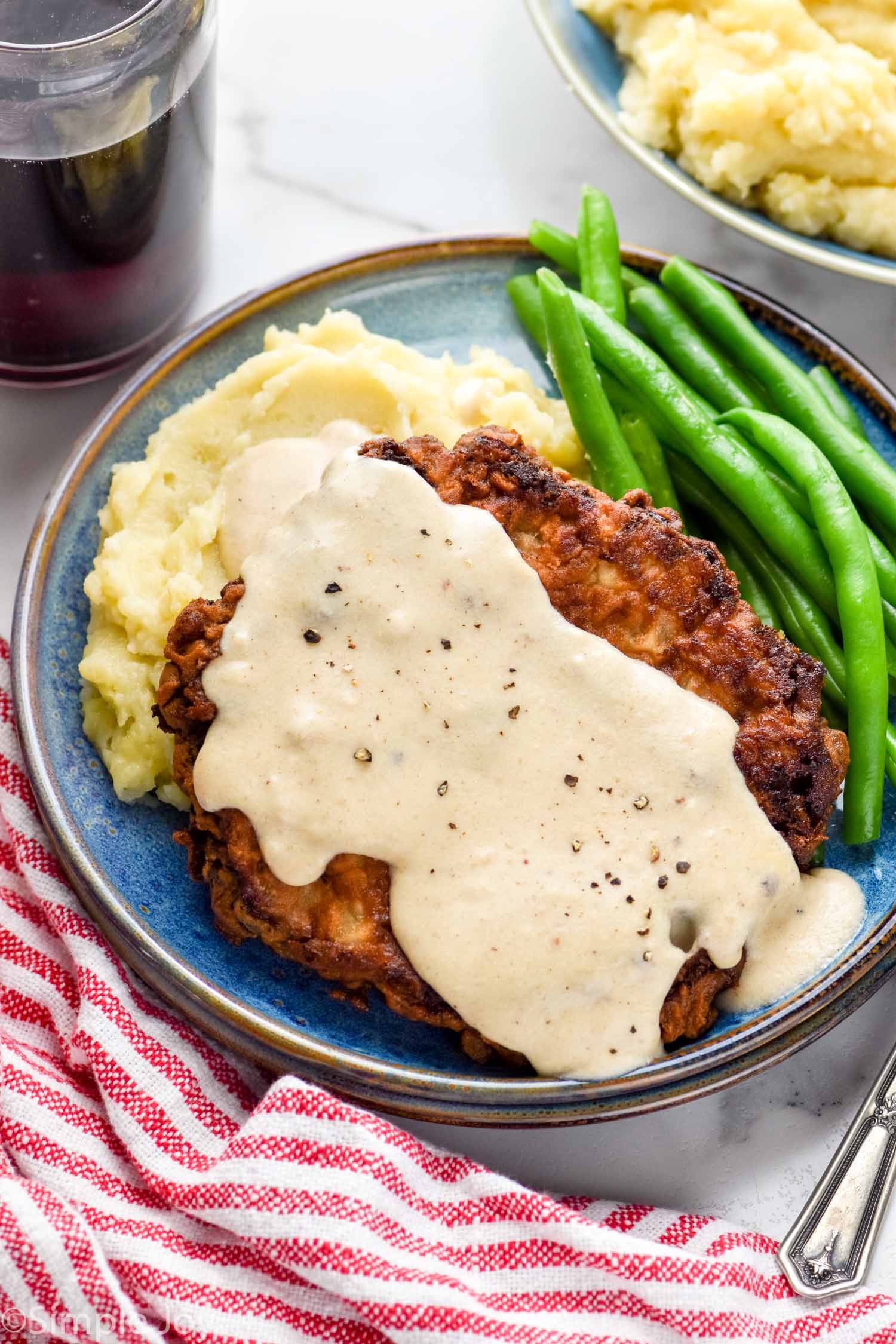 Chicken Fried Steak topped with country gravy on a plate with mashed potatoes and green beans