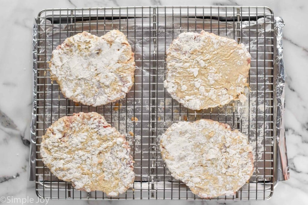 overhead of chicken fried steak on cooling rack on a foil lined baking sheet