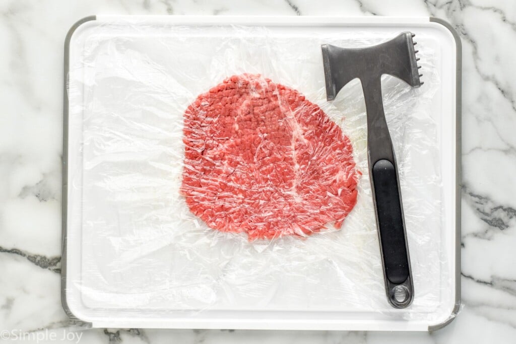 overhead of cutting board with cube steak and meat mallet for making Chicken Fried Steak