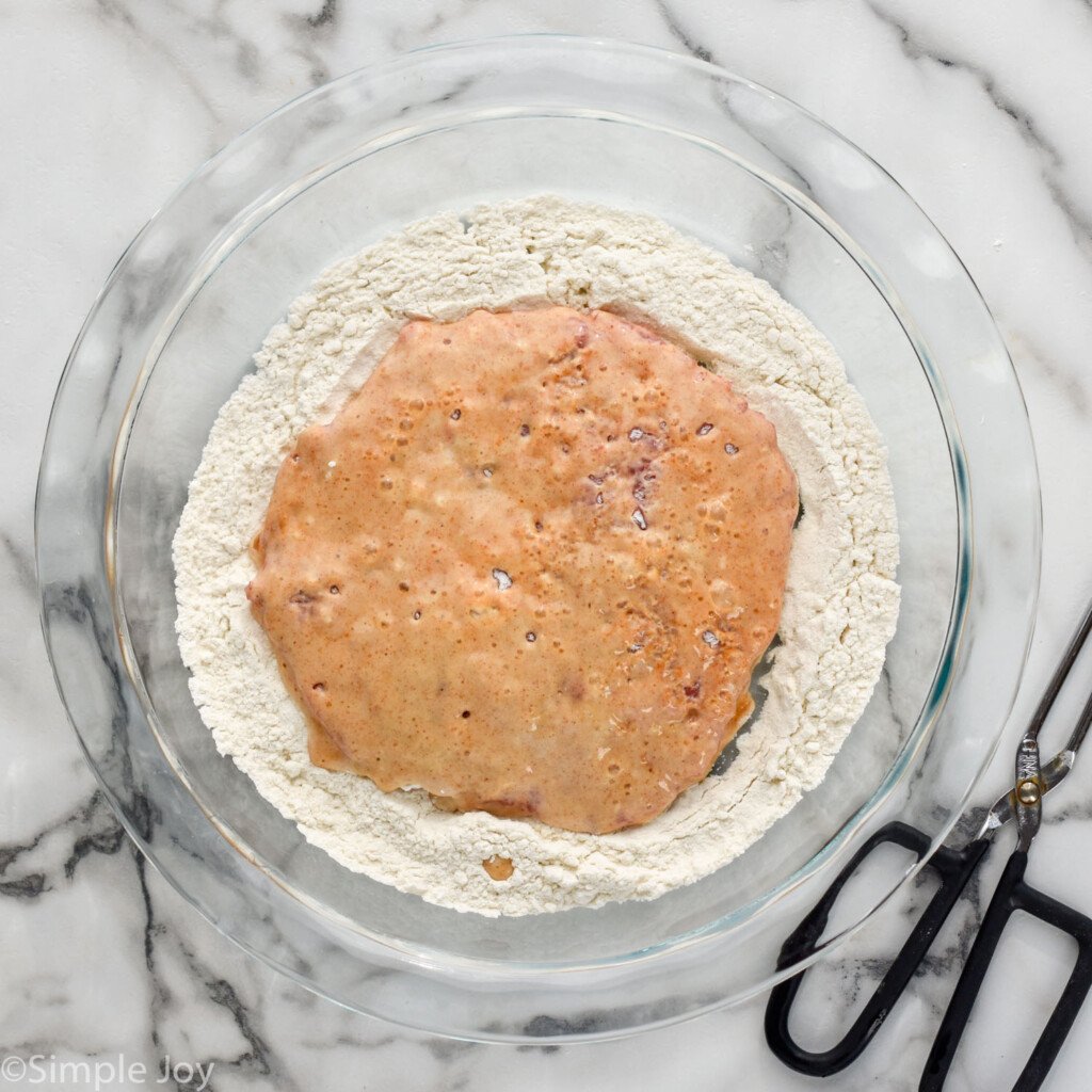 overhead of glass bowl of flour mixture with chicken fried steak, tongs sitting beside