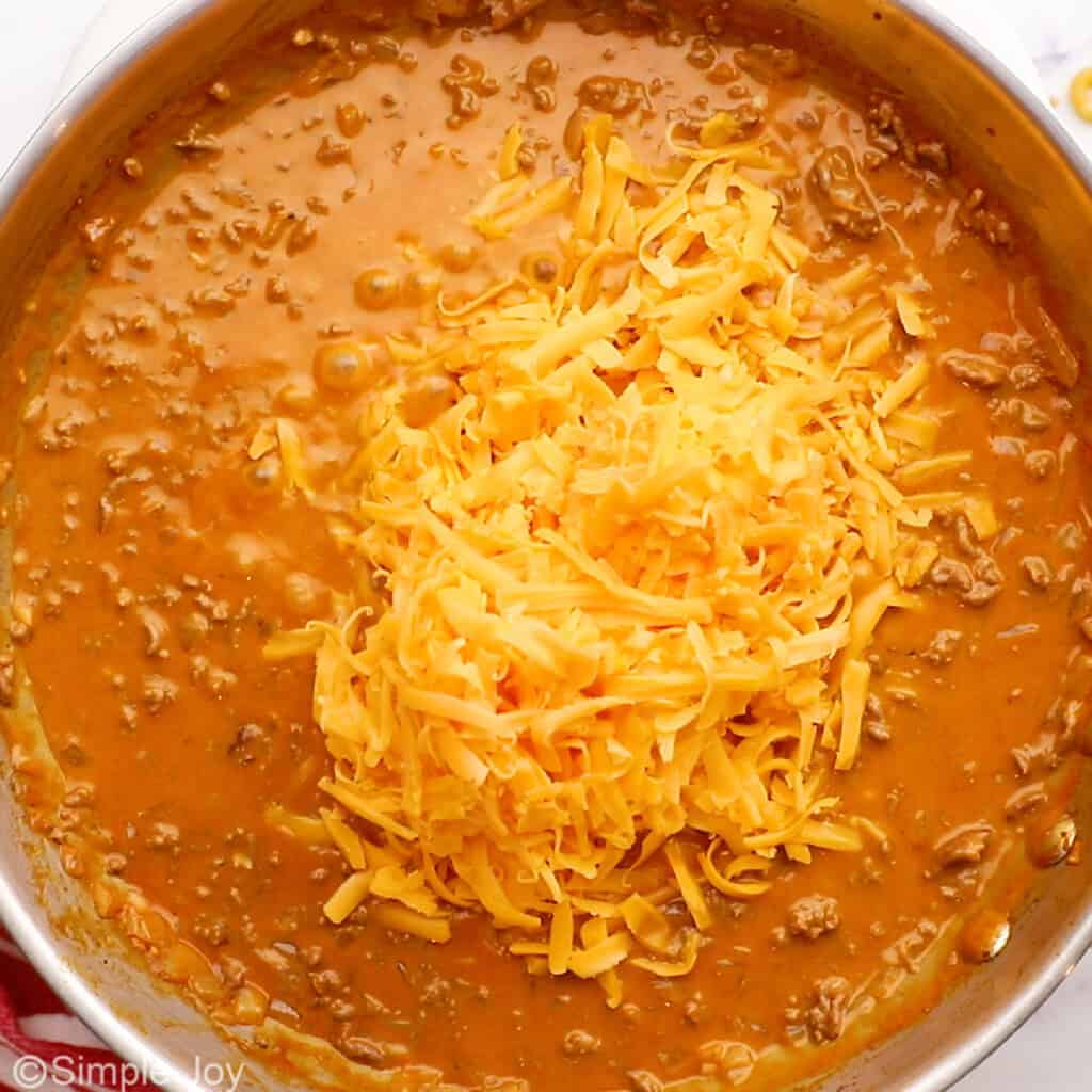 a pile of shredded cheddar cheese in a skillet with sauce and hamburger
