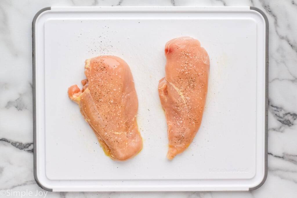 Overhead view of two raw seasoned chicken breasts on a cutting board for Instant Pot Chicken recipe.