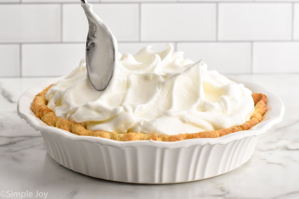 pie plate of Lemon Meringue Pie with spoon smoothing meringue swirls on top