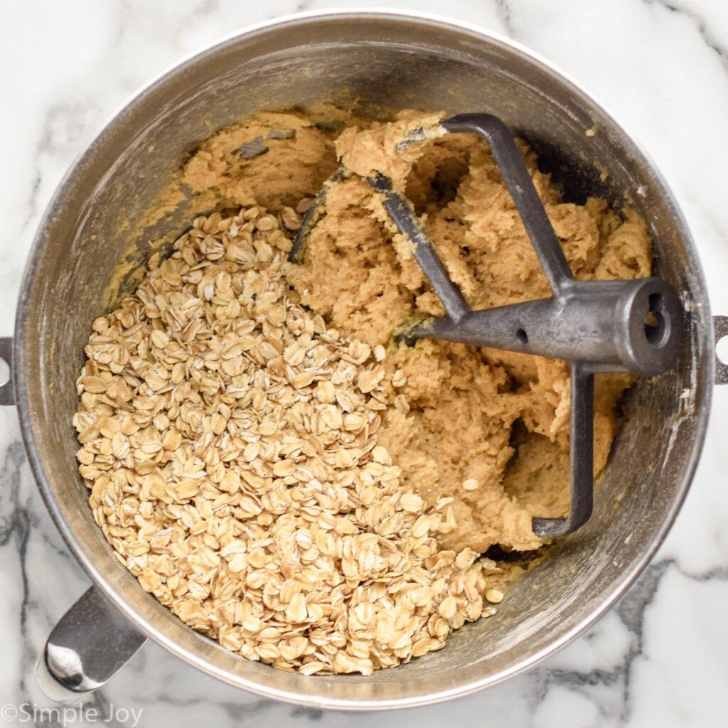overhead of mixing bowl of oatmeal cookie ingredients and paddle attachment
