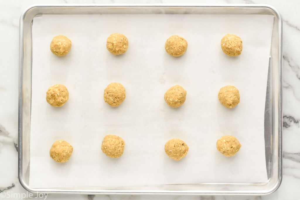overhead of oatmeal cookie dough balls on a parchment lined baking sheet to make oatmeal cookies.