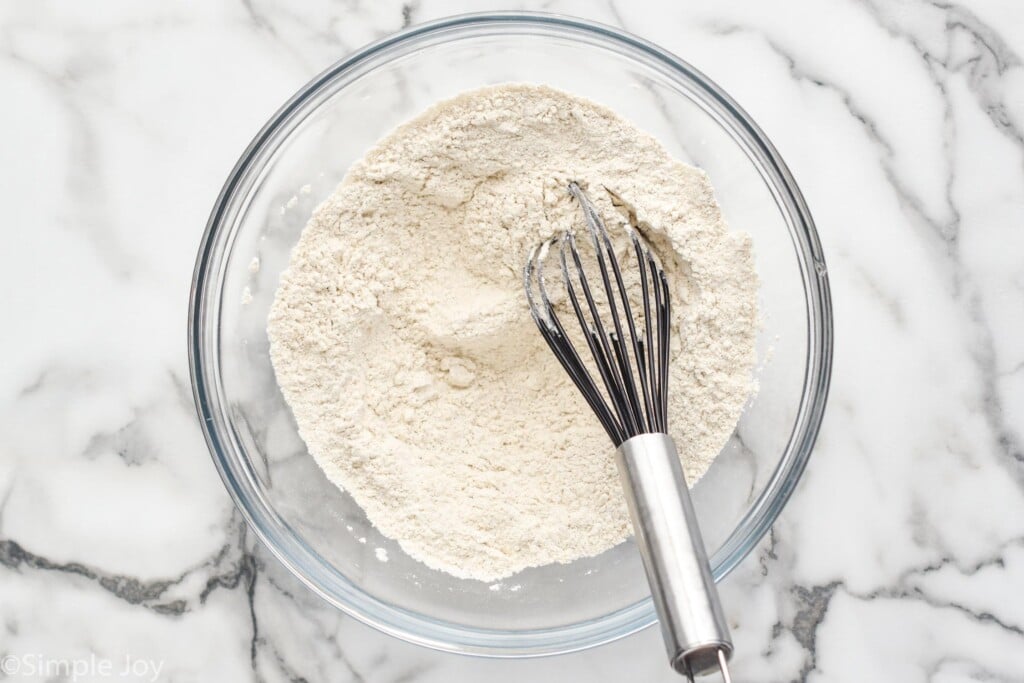 overhead of glass bowl of dry oatmeal cookie recipe ingredients and whisk to combine