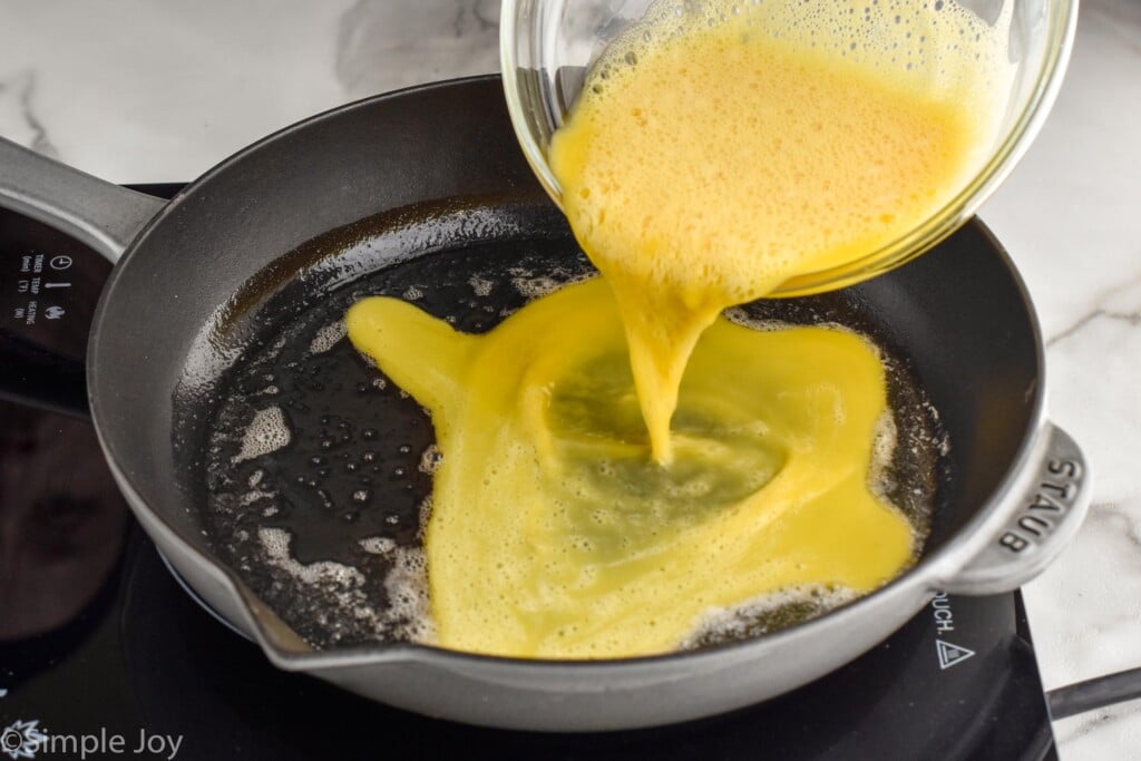glass bowl of eggs pouring into a skillet to make Scrambled Eggs