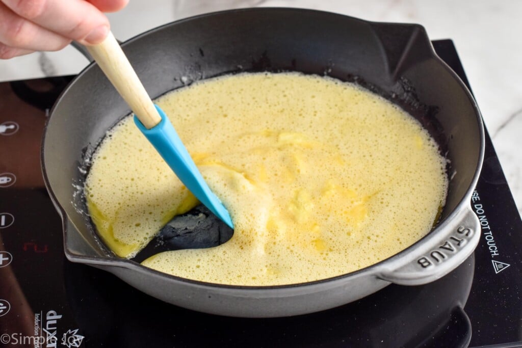 person's hand holding spatula in skillet and pulling eggs from the edge to make Scrambled Eggs