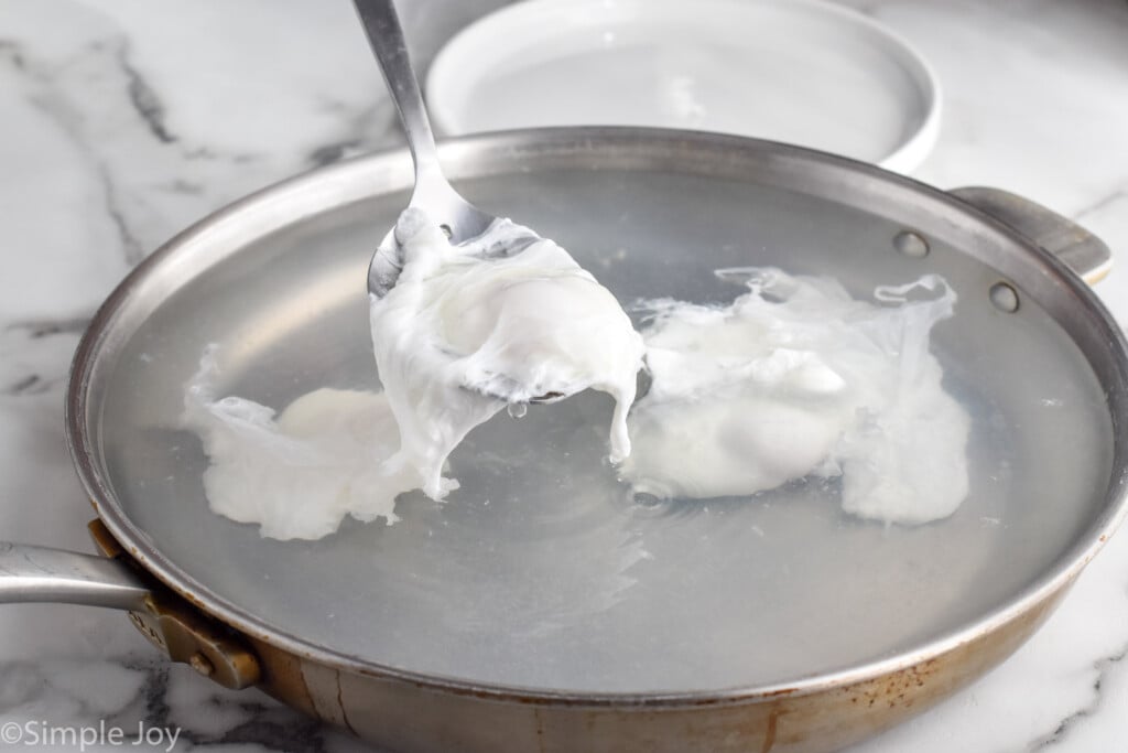 slotted spoon removing poached egg from skillet of water and other poached eggs