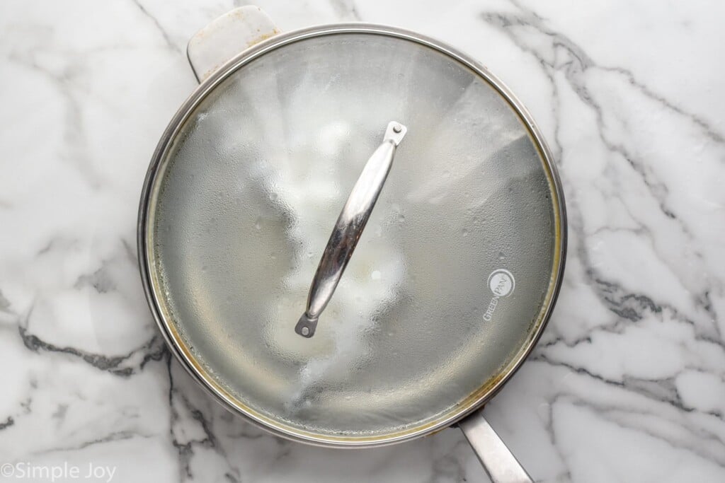 overhead of skillet of poached eggs cooking in water with lid on top