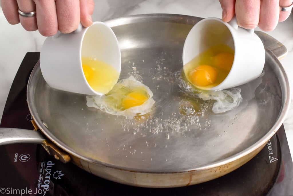 person's hands pouring two teacups of eggs into a skillet of water to make poached eggs