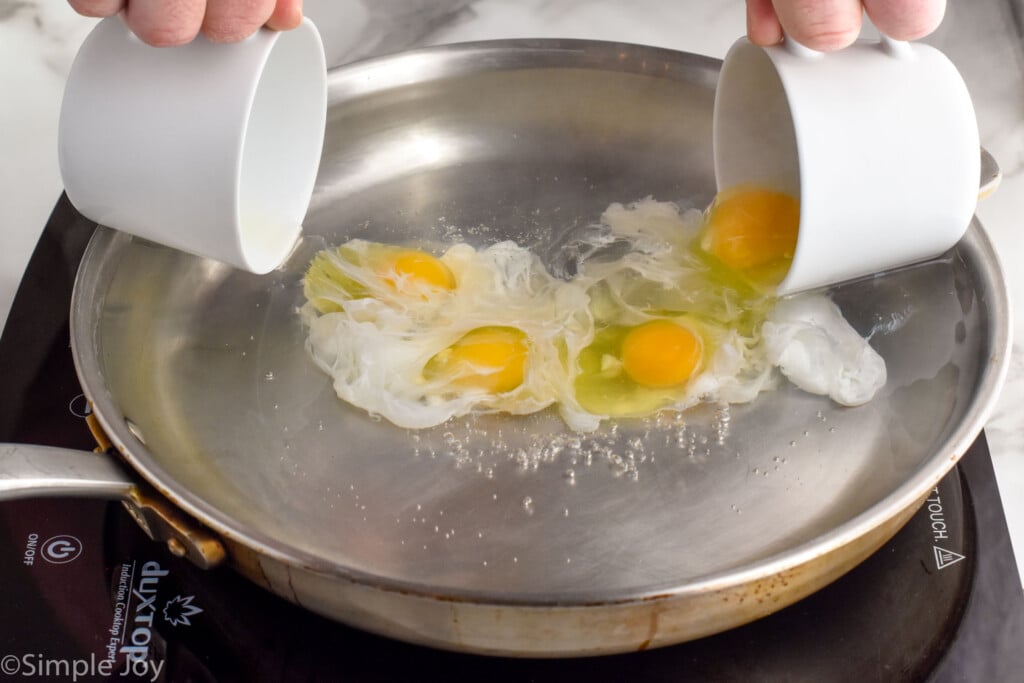 person's hands pouring two teacups of eggs into a skillet of water to make poached eggs