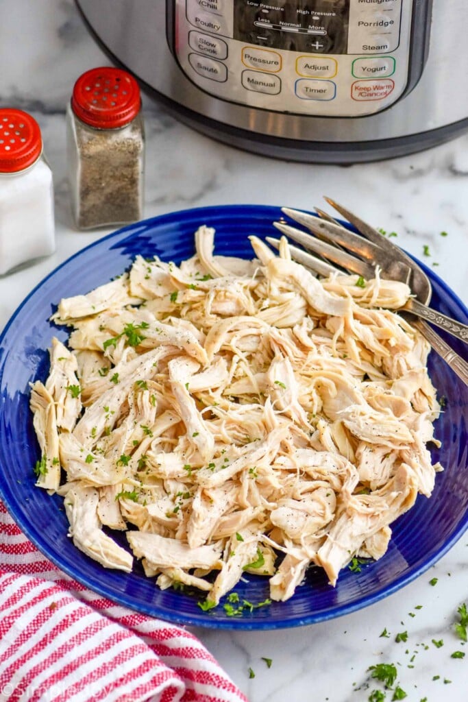 Plate of shredded Instant Pot Chicken recipe with forks. Seasonings and instant pot beside.