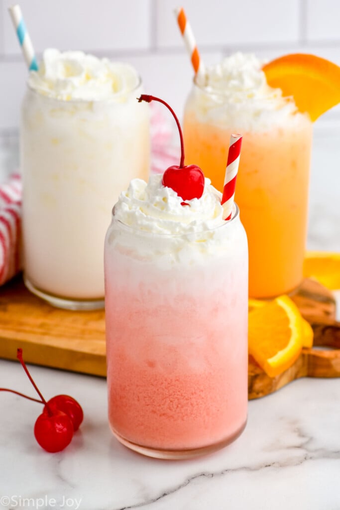Three glasses of Italian Soda and ice topped with whipped cream and fruit