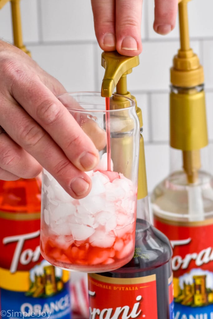 man's hand pumping flavored syrup into a glass of ice to make Italian Soda