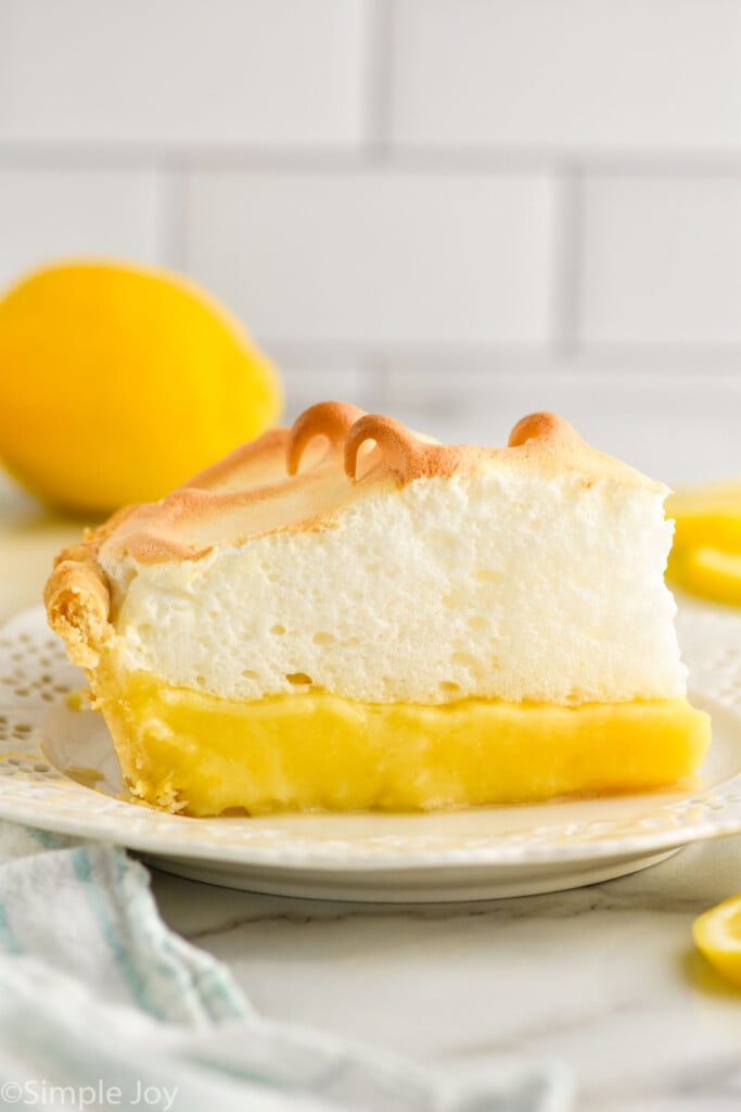 piece of Lemon Meringue Pie sitting on a plate. Lemon sitting in background