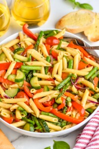 Bowl of Pasta Primavera with forks for serving. Bread and glasses of white wine beside.