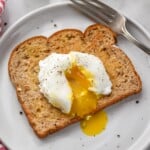 Poached Egg on a piece of buttered toast on a plate with a fork sitting beside - 11
