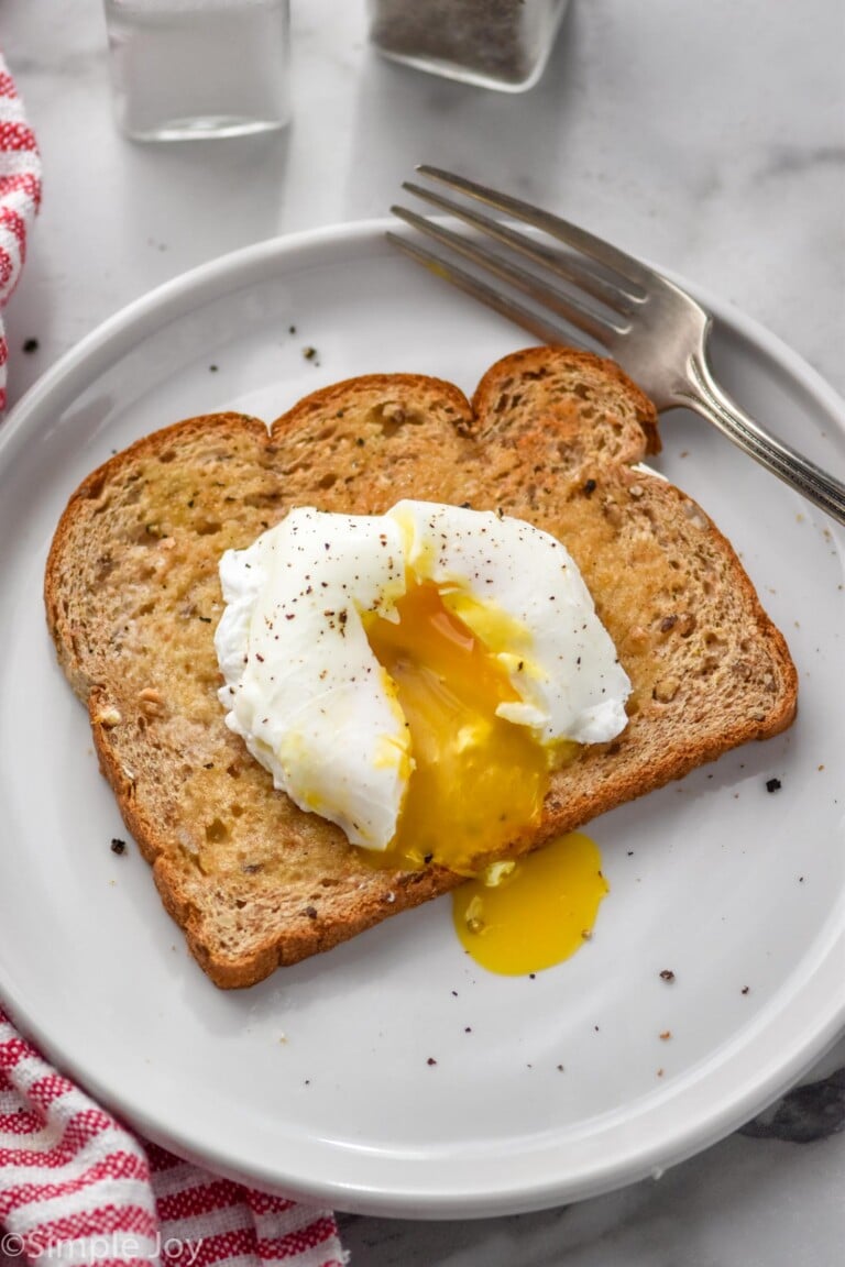 Poached Egg on a piece of buttered toast on a plate with a fork sitting beside