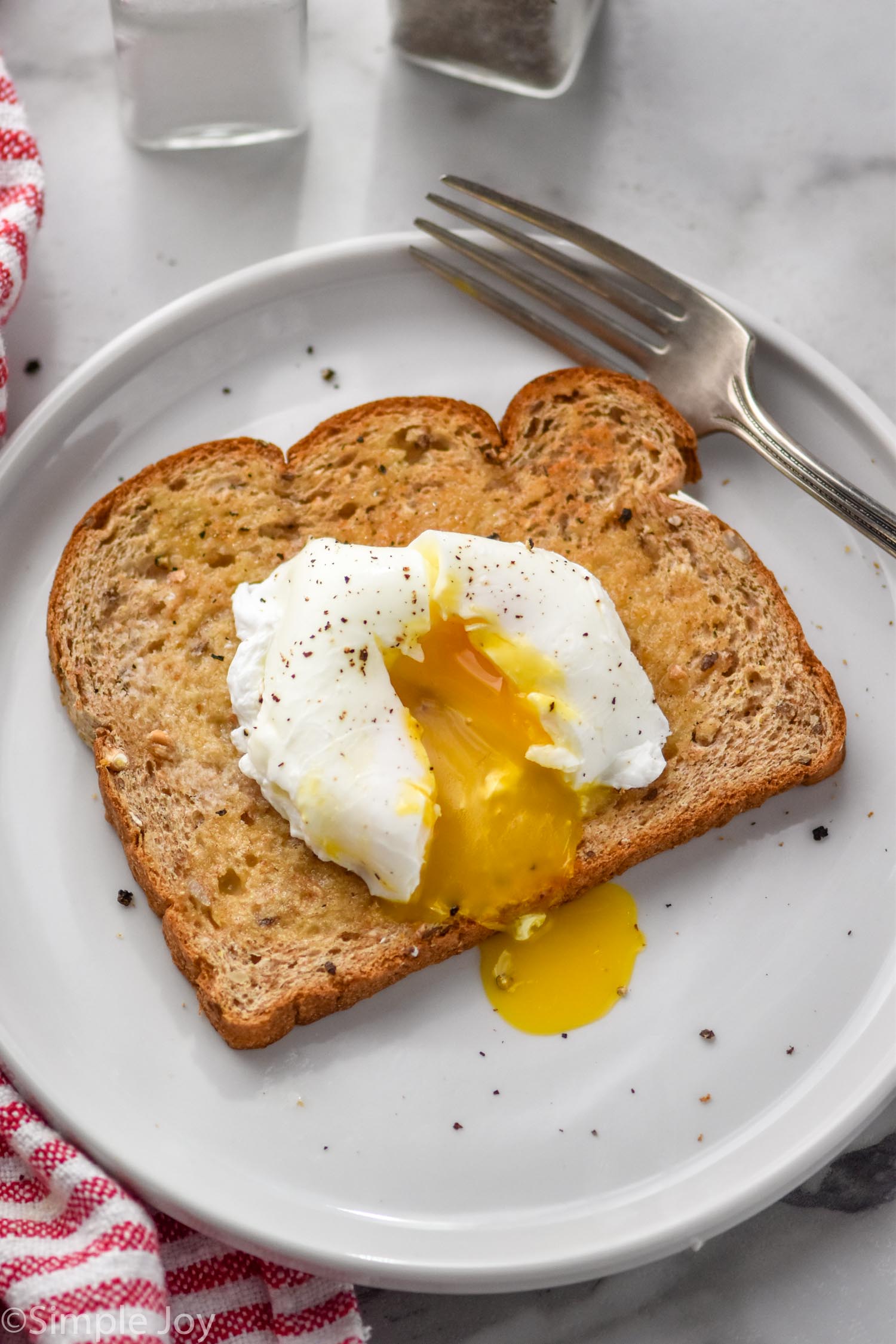 Poached Egg on a piece of buttered toast on a plate with a fork sitting beside