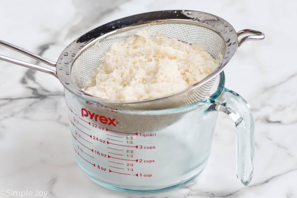 rinsed rice in a metal sieve over a glass measuring cup