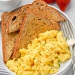 plate of Scrambled Eggs, pieces of toast, and a fork. Fresh strawberries and a mug of coffee sitting beside