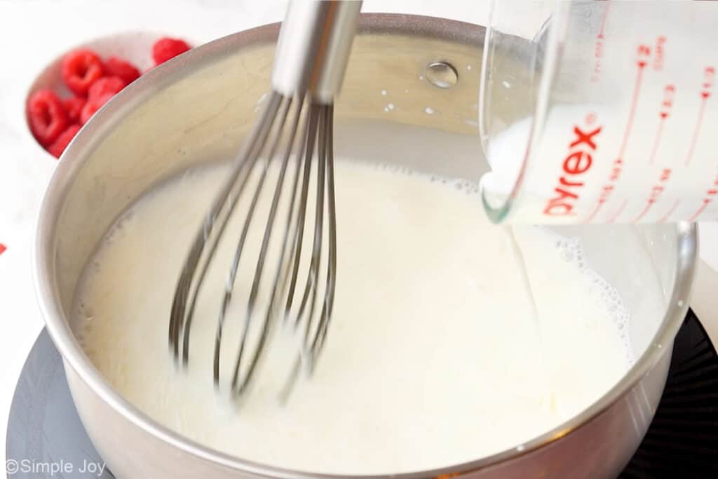 a small sauce pan with milk being poured into it and whisked