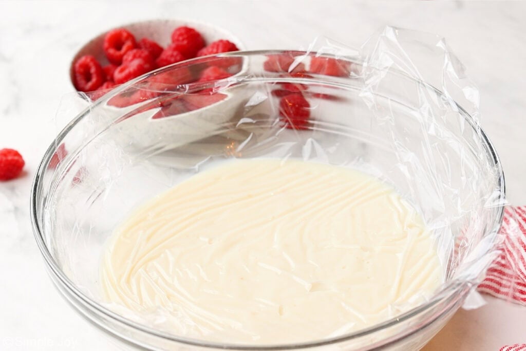 overhead of a glass bowl of vanilla pudding with plastic wrap pressed against the surface of the pudding