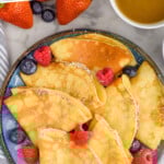 Pinterest graphic for Crepe Recipe. Says "simple and easy Crepe Recipe simplejoy.com" Image shows a plate of crepes topped with powdered sugar and fresh raspberries and blueberries.