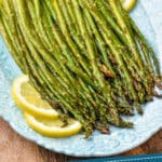 pinterest graphic of side view of asparagus made in the oven on a blue platter garnished with lemon slices that says "oven roasted asparagus simplejoy.com"