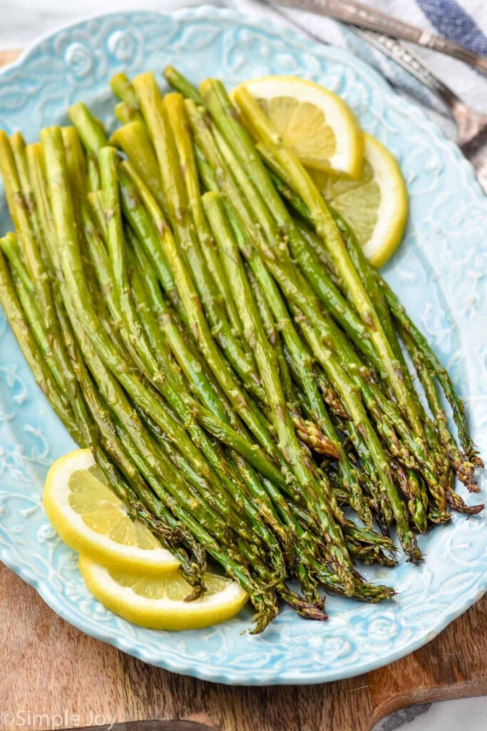 side view of asparagus made in the oven on a blue platter garnished with lemon slices
