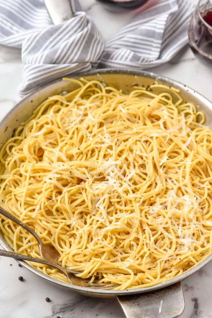 Skillet of Cacio E Pepe topped with black pepper and grated cheese with two forks
