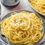 Plate of Cacio E Pepe topped with ground black pepper and grated cheese. Glass of red wine and skillet of Cacio E Pepe sitting in background. - 9