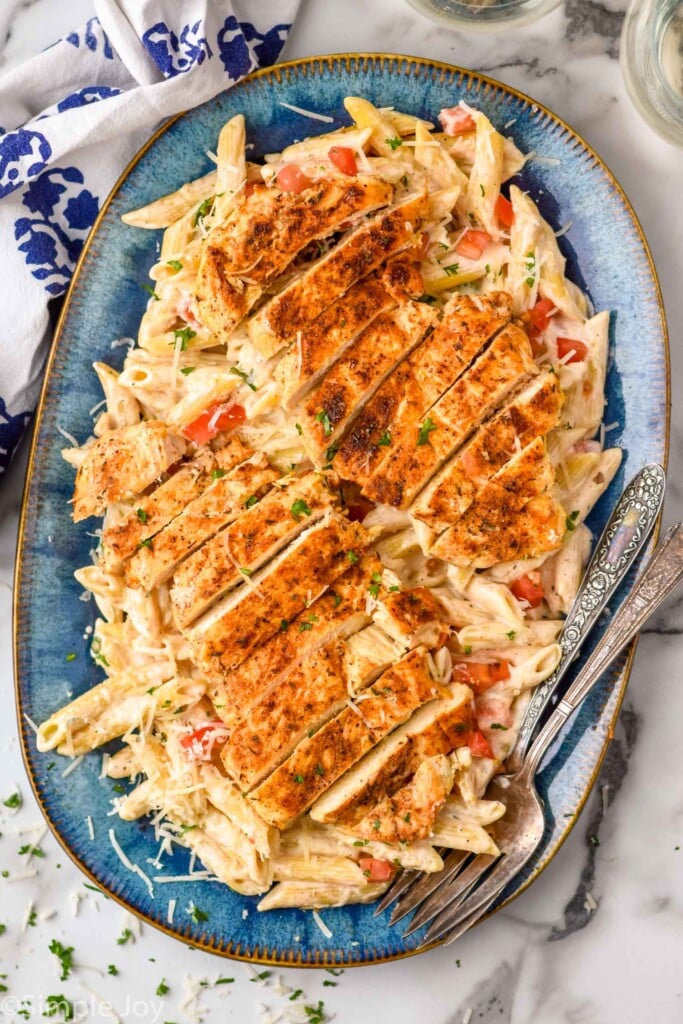 Overhead view of a platter of Creamy Cajun Chicken Pasta with forks for serving. Garnished with shredded parmesan cheese and parsley.