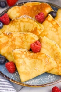 Plate of crepes topped with powdered sugar and fresh berries