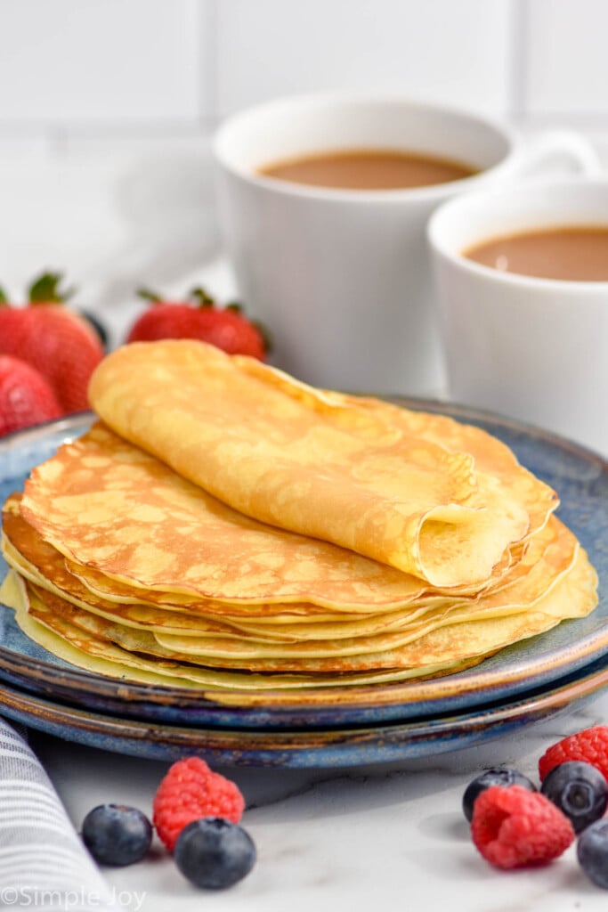 Plate of stack of crepes. Fresh berries and two mugs of coffee sitting behind