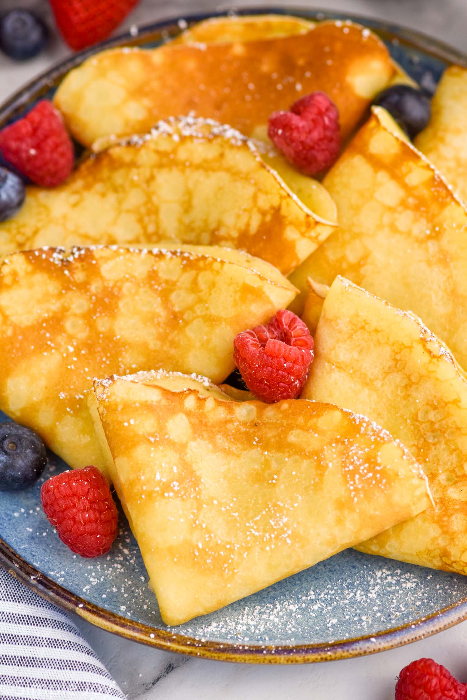 Plate of crepes topped with powdered sugar and fresh berries