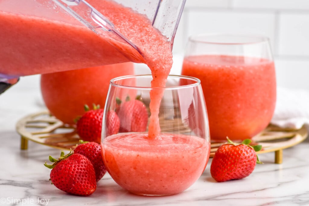 blender of strawberry daiquiri pouring into a glass. Two glasses of daiquiri strawberry and fresh strawberries sitting in background