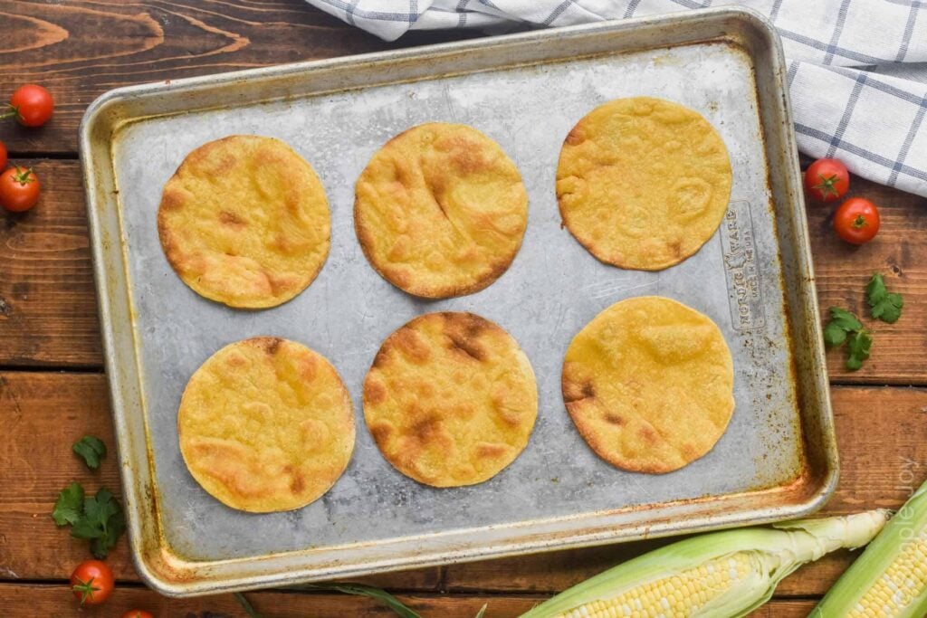 overhead photo of a rimmed baking sheet with six corn tortillas that have been baked to make homemade tostadas